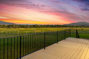 Deck at dusk with a mountain view, a yard, and a rural view