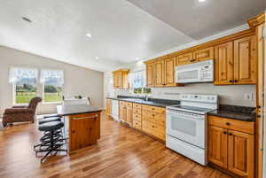 Kitchen with white appliances, a kitchen breakfast bar, a kitchen island, lofted ceiling, and light hardwood / wood-style floors