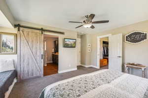 Carpeted bedroom featuring a walk in closet, a closet, connected bathroom, a barn door, and ceiling fan