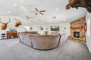 Living room featuring vaulted ceiling, carpet floors, ceiling fan, and a stone fireplace