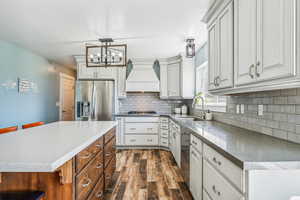 Kitchen with pendant lighting, appliances with stainless steel finishes, sink, custom exhaust hood, and white cabinets