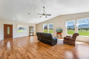 Living room with ceiling fan, vaulted ceiling, and light hardwood / wood-style floors