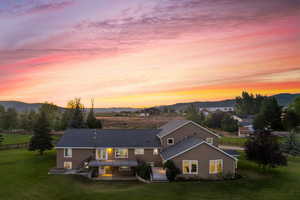 Back house at dusk featuring a lawn, a patio, and a mountain view