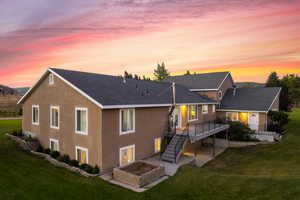 Back house at dusk featuring a lawn, a wooden deck, and a patio