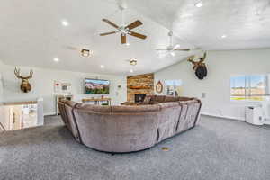 Living room featuring dark carpet, ceiling fan, a stone fireplace, and vaulted ceiling