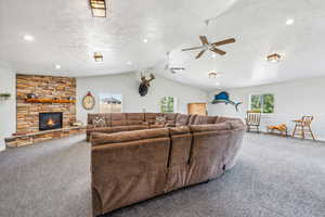 Carpeted living room featuring vaulted ceiling, a healthy amount of sunlight, ceiling fan, and a stone fireplace