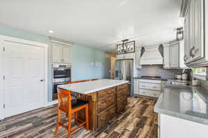 Kitchen with a center island, custom exhaust hood, dark hardwood / wood-style flooring, stainless steel appliances, and sink