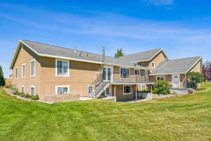 Back of property featuring a wooden deck, a lawn, and a patio