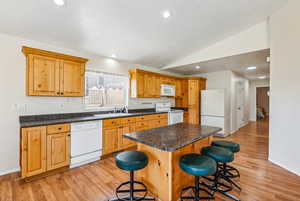 Kitchen with lofted ceiling, white appliances, a center island, and light wood-type flooring