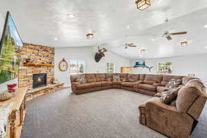 Carpeted living room featuring lofted ceiling, ceiling fan, a textured ceiling, and a stone fireplace