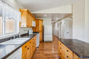 Kitchen featuring white appliances, light hardwood / wood-style flooring, sink, and lofted ceiling