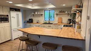 Kitchen featuring a breakfast bar, a raised ceiling, kitchen peninsula, butcher block countertops, and white fridge