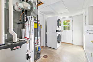 Washroom featuring water heater, heating unit, and stacked washer / dryer and outside exit