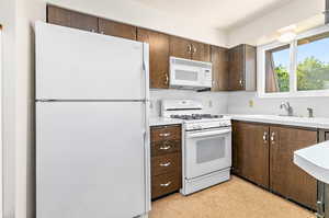 Kitchen with sink, dark brown cabinetry, and white appliances