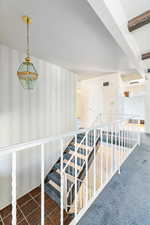 Stairway with dark colored carpet and an inviting chandelier