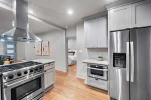 Kitchen with gray cabinets, light hardwood / wood-style flooring, stainless steel appliances, range hood, and light stone countertops