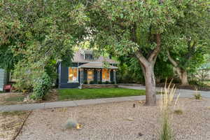 View of property hidden behind natural elements with a front lawn and a porch