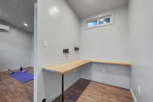 Office featuring built in desk, a wall unit AC, and light hardwood / wood-style floors