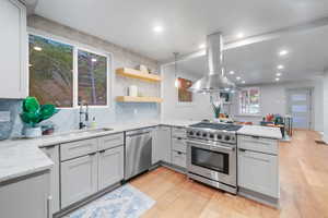 Kitchen featuring light wood-type flooring, island exhaust hood, sink, light stone countertops, and appliances with stainless steel finishes