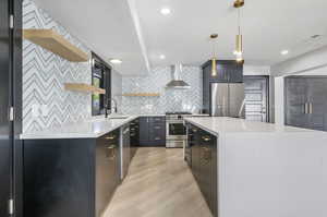 Kitchen with hanging light fixtures, light wood-type flooring, stainless steel appliances, sink, and wall chimney exhaust hood