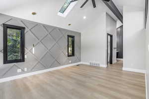 Empty room featuring light hardwood / wood-style flooring, ceiling fan, and lofted ceiling with skylight