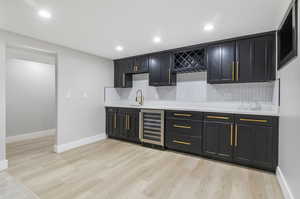 Kitchen with beverage cooler, sink, tasteful backsplash, and light hardwood / wood-style floors