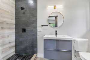 Bathroom with wood-type flooring, toilet, a tile shower, and vanity