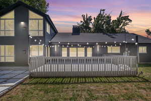 Back house at dusk featuring a deck and a lawn