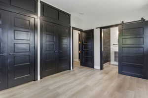 Unfurnished bedroom featuring a barn door and light hardwood / wood-style floors