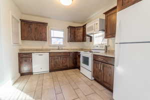 Kitchen with sink, light tile patterned floors, light stone counters, and white appliances