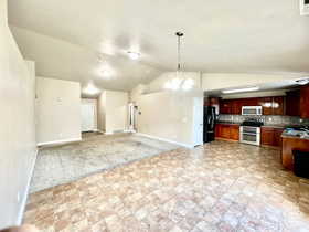 Kitchen with black fridge, stove, decorative light fixtures, vaulted ceiling, and decorative backsplash