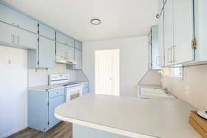 Kitchen featuring dark wood-type flooring, sink, kitchen peninsula, white electric range oven, and blue cabinetry