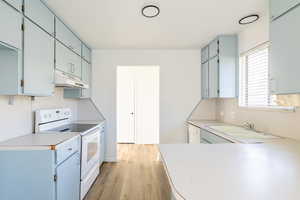 Kitchen with blue cabinets, white electric range, light hardwood / wood-style flooring, and sink