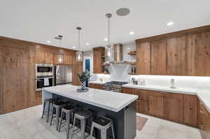 Kitchen with a center island, decorative light fixtures, stainless steel appliances, extractor fan, and a breakfast bar area