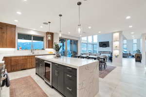 Kitchen with light stone countertops, beverage cooler, a center island, hanging light fixtures, and sink