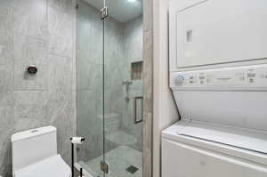 Bathroom with tile walls, walk in shower, toilet, and stacked washer / dryer