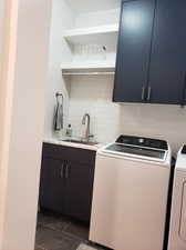 Washroom with dark tile patterned floors, washing machine and clothes dryer, cabinets, and sink