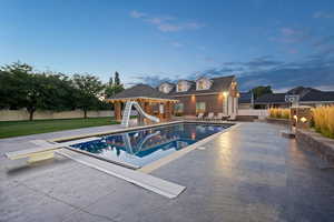 Pool at dusk featuring a patio, a gazebo, a lawn, a water slide, and a diving board