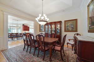 Dining room with a notable chandelier, light hardwood / wood-style flooring, a raised ceiling, and ornamental molding