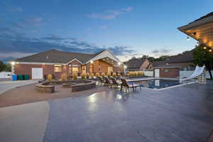 Pool at dusk with a water slide, a patio area, and an outdoor fire pit