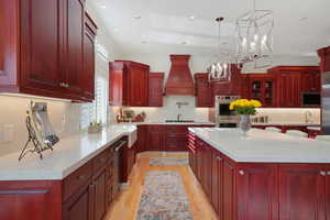 Kitchen with custom range hood, appliances with stainless steel finishes, an inviting chandelier, a center island, and decorative light fixtures