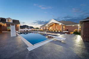 Pool at dusk with a patio, a diving board, and a water slide