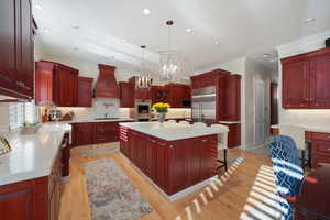 Kitchen featuring pendant lighting, custom exhaust hood, a kitchen island, stainless steel appliances, and light wood-type flooring