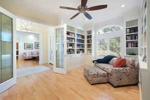 Living area with ceiling fan with notable chandelier, built in shelves, hardwood / wood-style floors, and crown molding