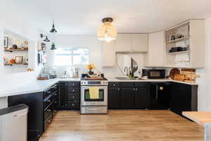 Kitchen with white cabinets, light wood-type flooring, black appliances, an inviting chandelier, and decorative light fixtures