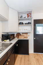 Kitchen with black appliances, a textured ceiling, light wood-type flooring, and white cabinetry