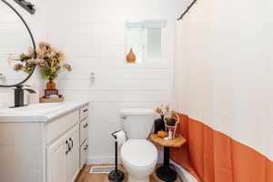 Bathroom with vanity, toilet, curtained shower, wooden walls, and hardwood / wood-style floors