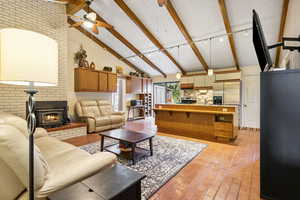 Living room featuring a fireplace, ceiling fan, brick wall, high vaulted ceiling, and beam ceiling