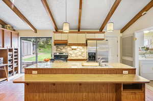 Kitchen featuring independent washer and dryer, hanging light fixtures, vaulted ceiling with beams, appliances with stainless steel finishes, and a center island with sink