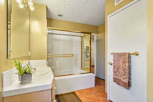 Bathroom with tile patterned flooring, enclosed tub / shower combo, a textured ceiling, and vanity